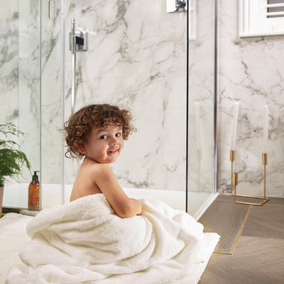 Boy sat on bathroom floor wrapped in a towel
