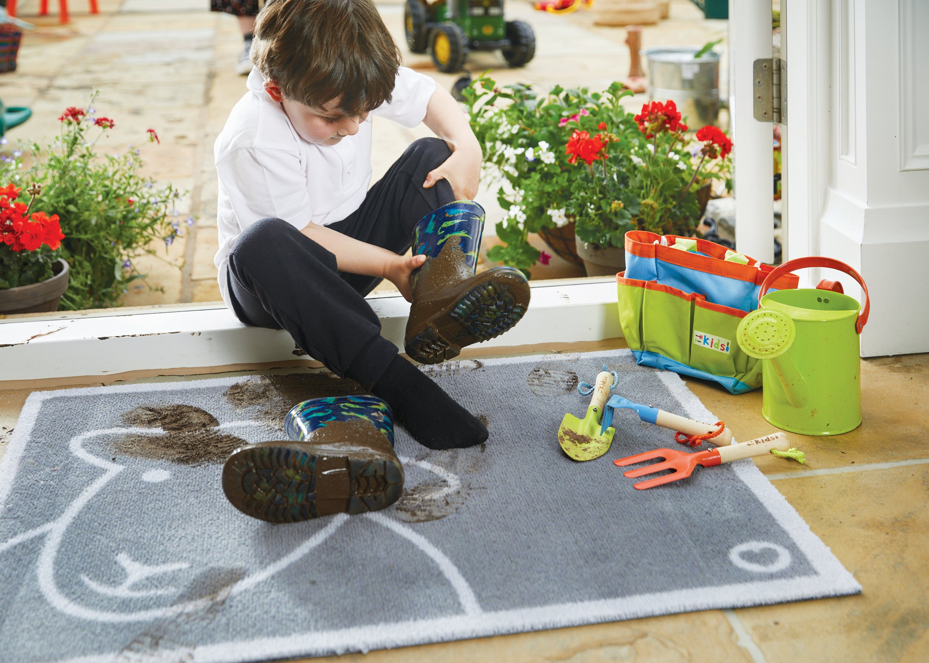 Young boy taking off muddy boots on a Hello Herdy mat