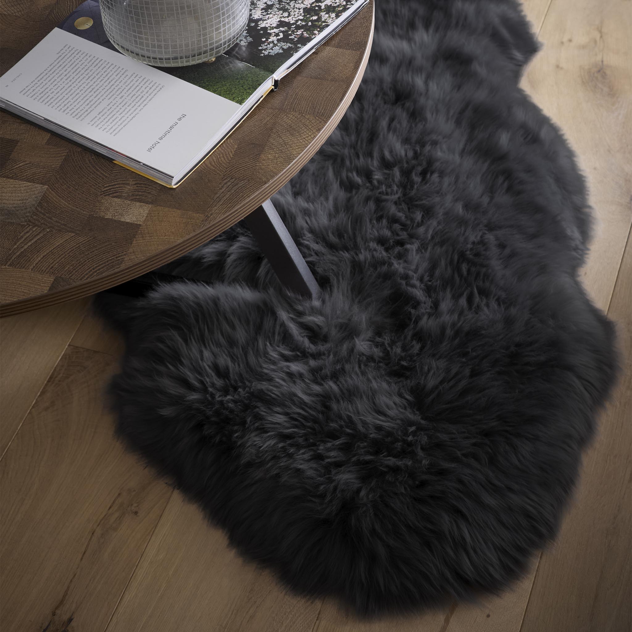 Black fluffy sheepskin rug under a coffee table on an oak floor.