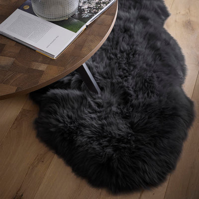 Black fluffy sheepskin rug under a coffee table on an oak floor.