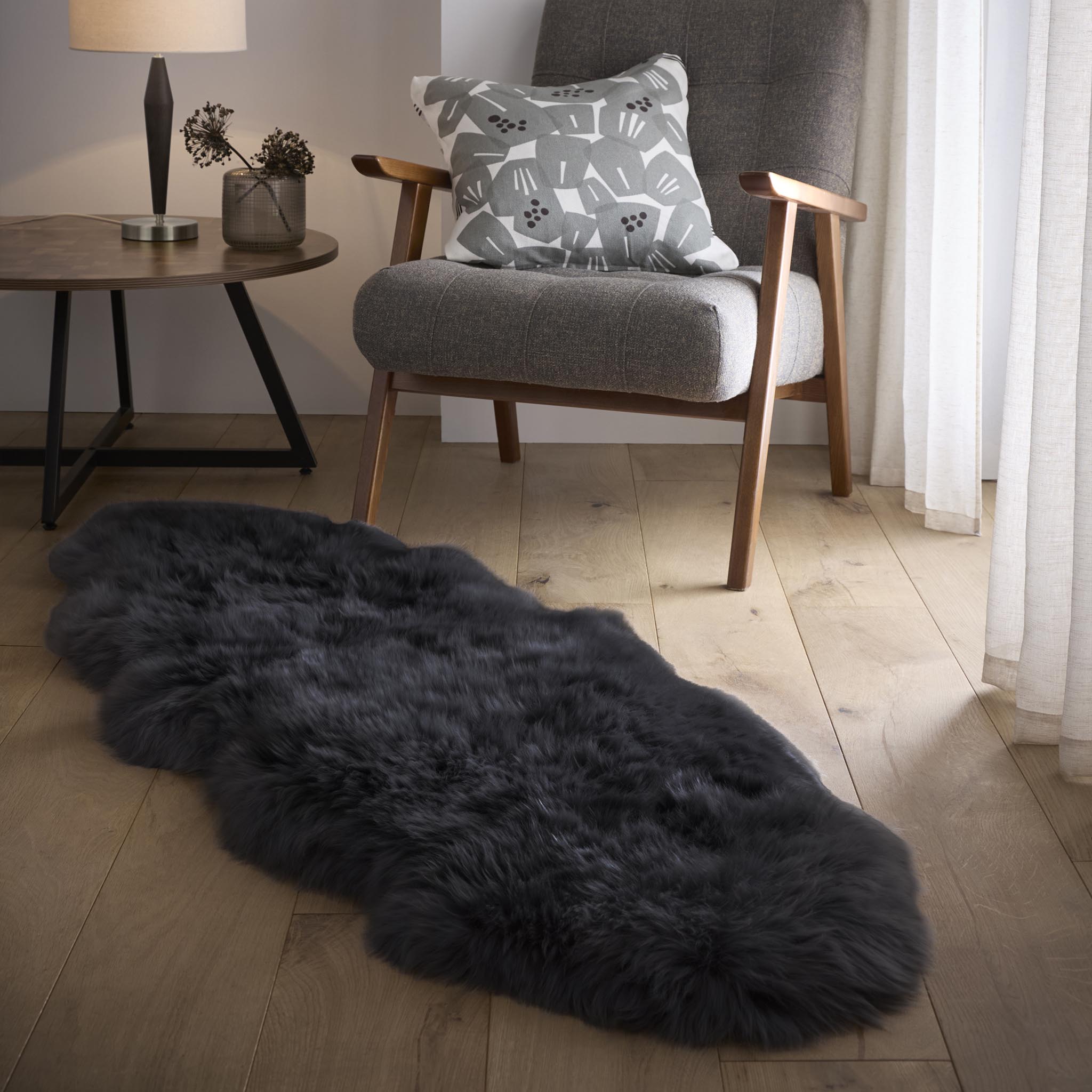 Plush black double sheepskin rug on a wooden floor with a chair and side table in the background.
