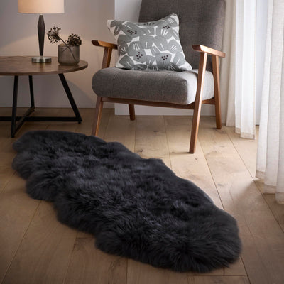 Plush black double sheepskin rug on a wooden floor with a chair and side table in the background.