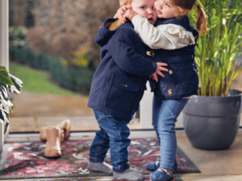 Two young children hugging each other at the front door of a home