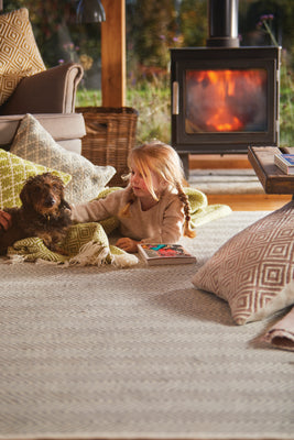 A dog and a young girl lying in front of a fire on a rug