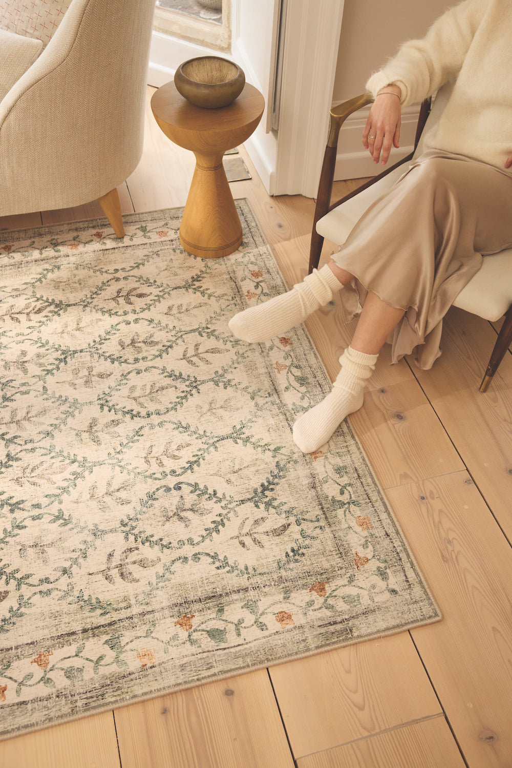 An English Garden Washable rug on a wooden floor, with a woman relaxing in a chair