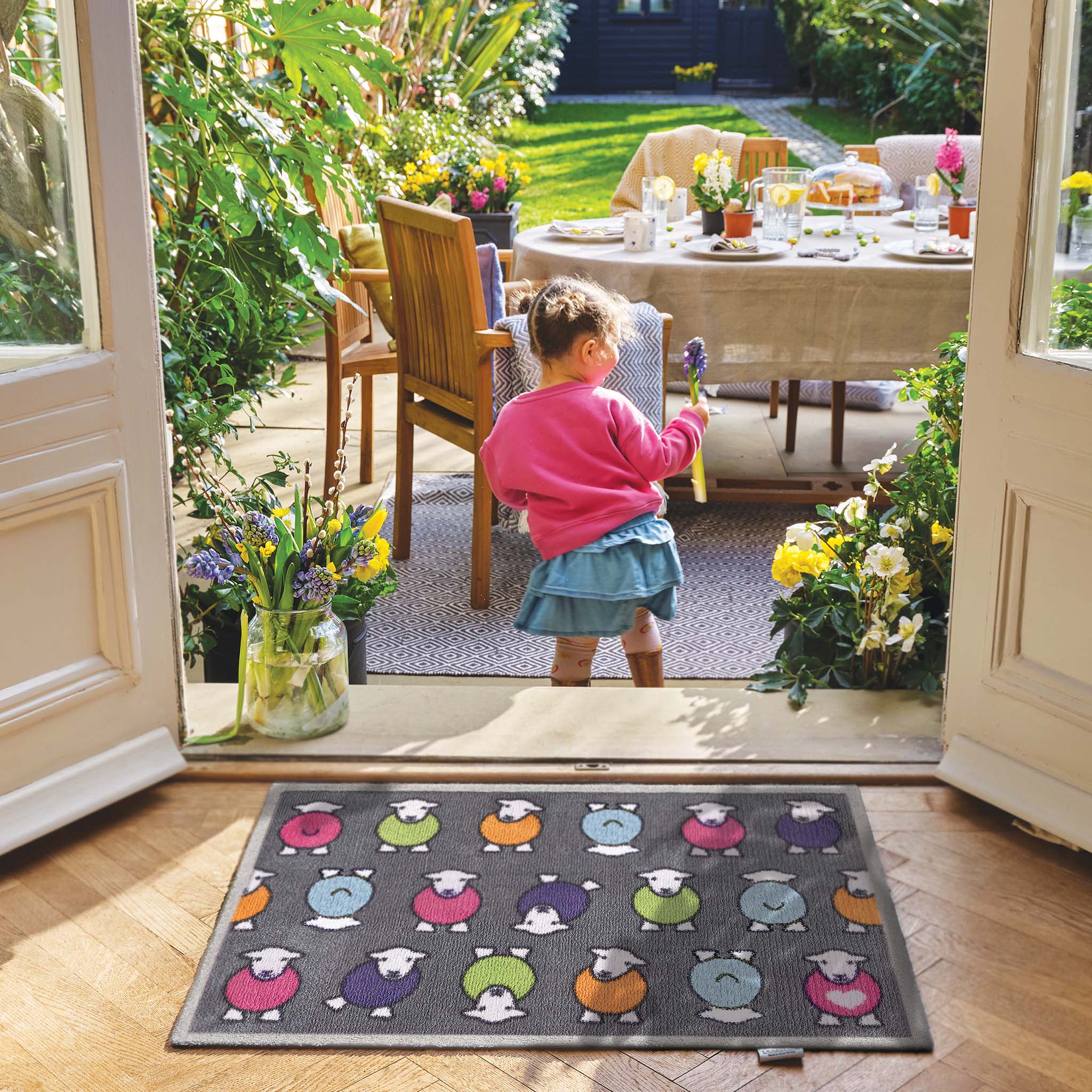 Lifestyle image of a young girl stood in front of a grey marra Herdy washable doormat from Hug Rug