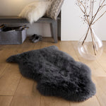 Plush black single sheepskin rug on a wooden floor.