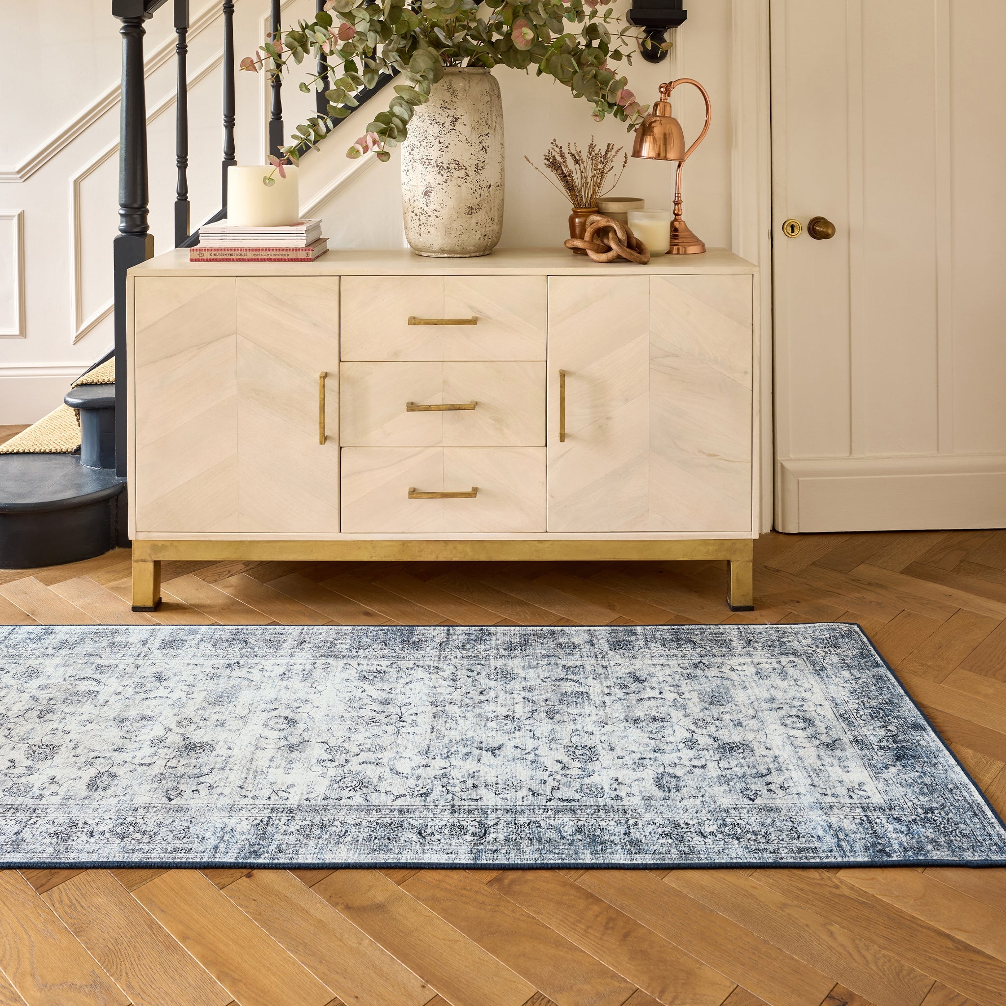 Hallway showing a runner in a vintage blue and grey pattern on wooden floor with a cabinet in the background 