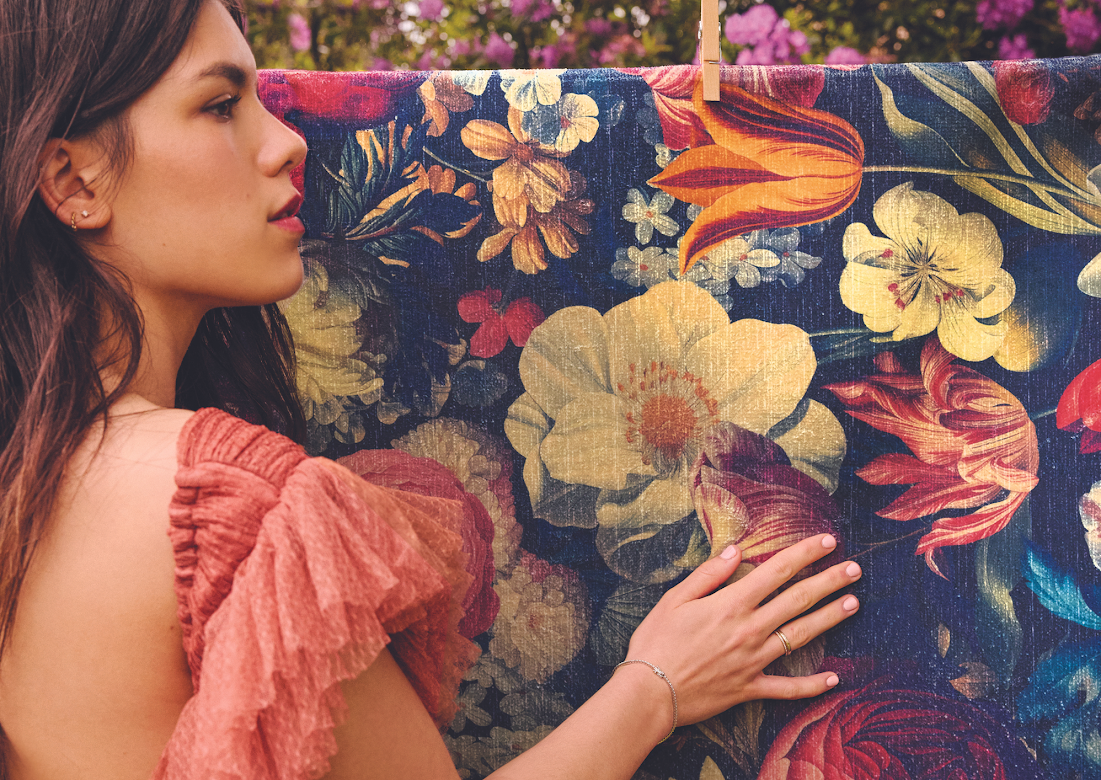 Young woman with her hand placed on a Dark Floral Eco Washable rug in a flowery garden